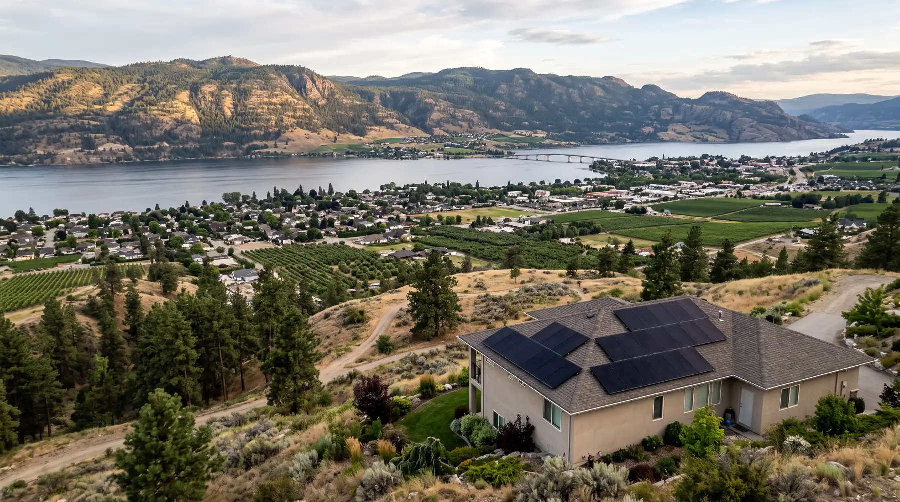 Panorama of Kelowna from a hillside with Okanagan Lake, the bridge, orchards and a solar home in the foreground