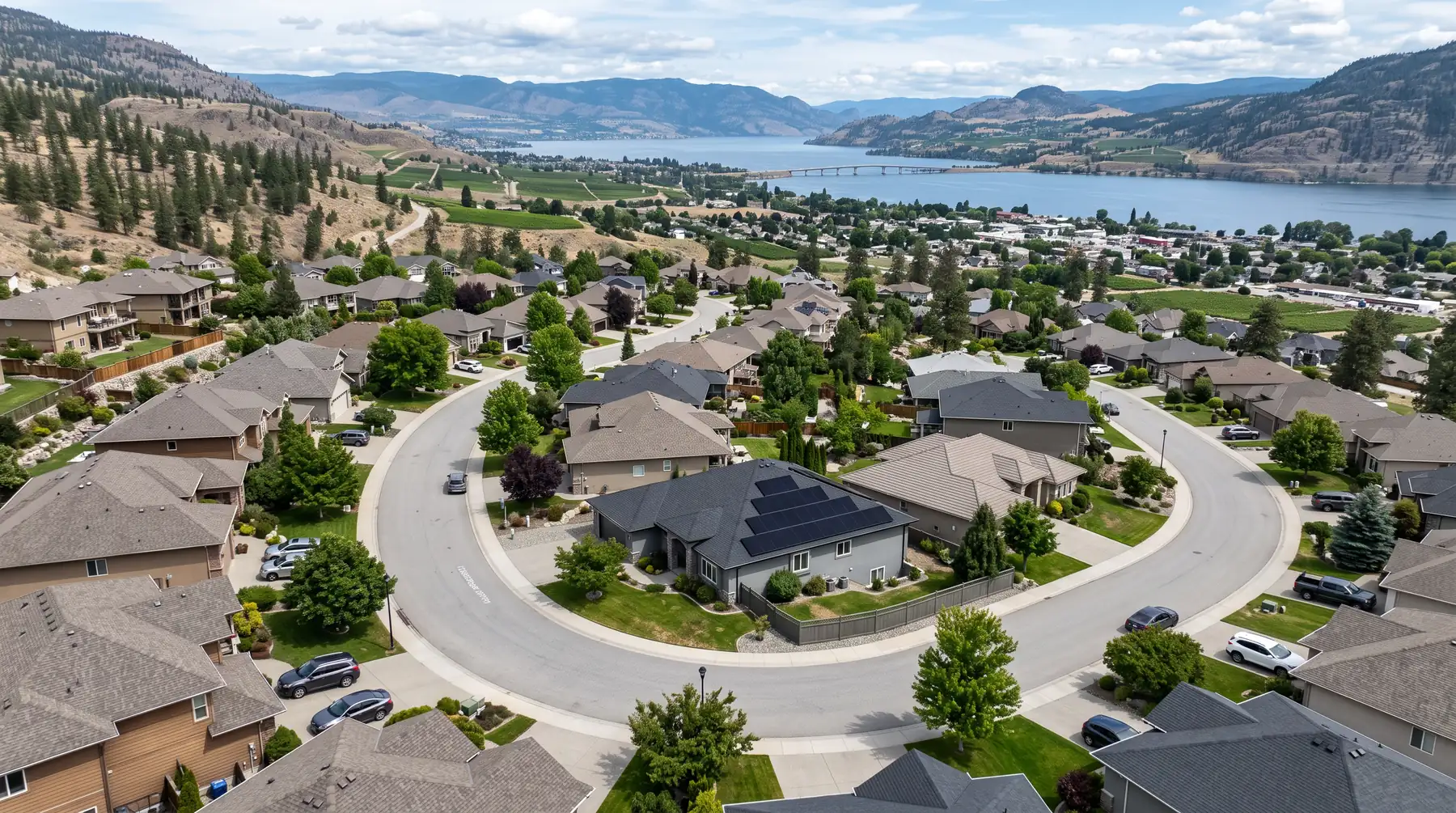 Aerial view of a Kelowna neighbourhood with one home carrying a black solar array, the lake in the distance